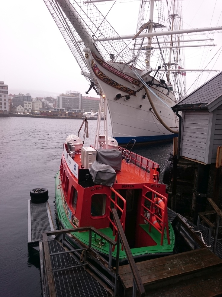 To get around Bergen, take the little green and orange boat dwarfed here by a tall ship across the Bergen harbor.
