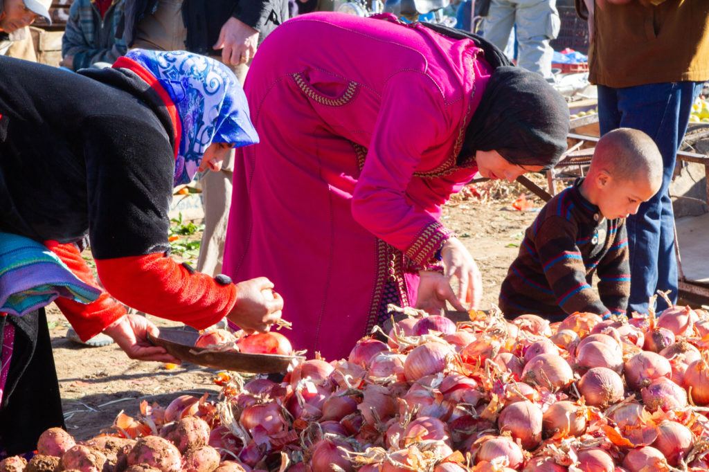 Women picking onions to buy from a pile at the Berber Market in Azrou, Morocco.