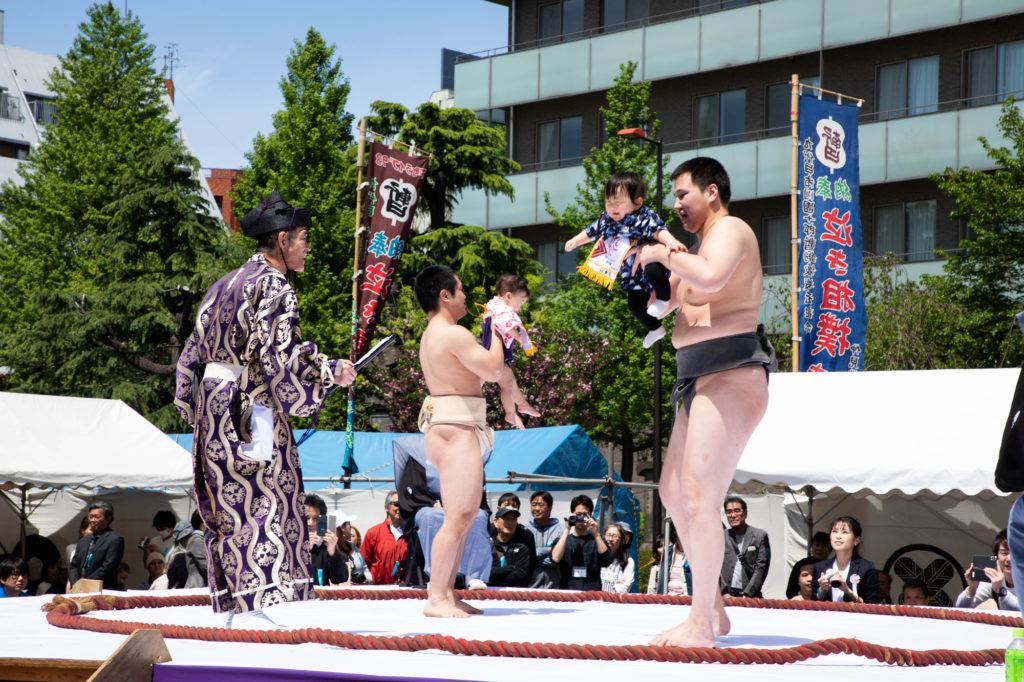Sumo wrestlers holds a crying baby.