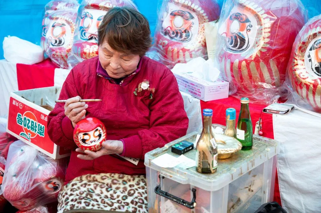 A vendor paints the prayer on the back of a Daruma.