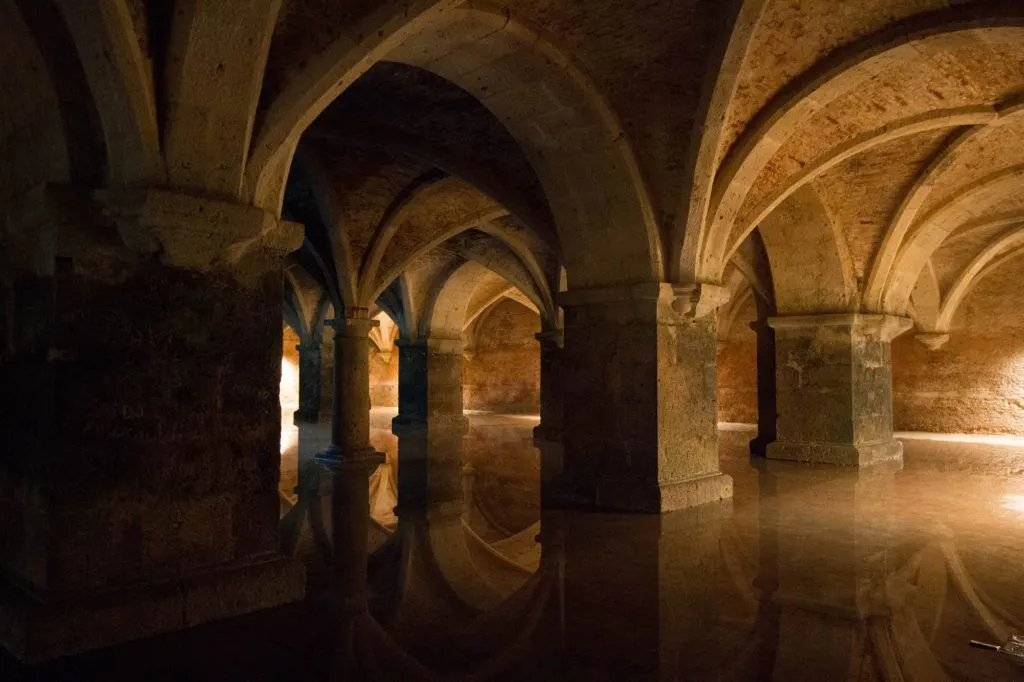 Underground cistern with stone pillars, rippling light, and sounds of dripping water.