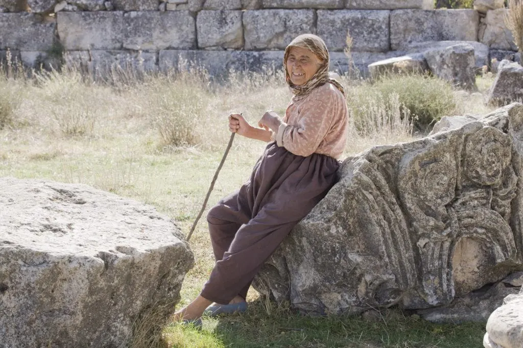 An older lady sits on downed columns watching her herd.
