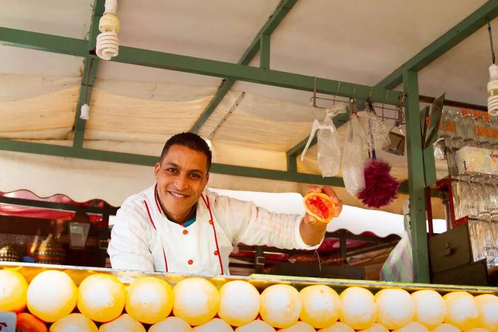 A Jemaa el Fna food stall vendor holds up half a grapefruit to show the freshness of his fresh-squeezed juice.