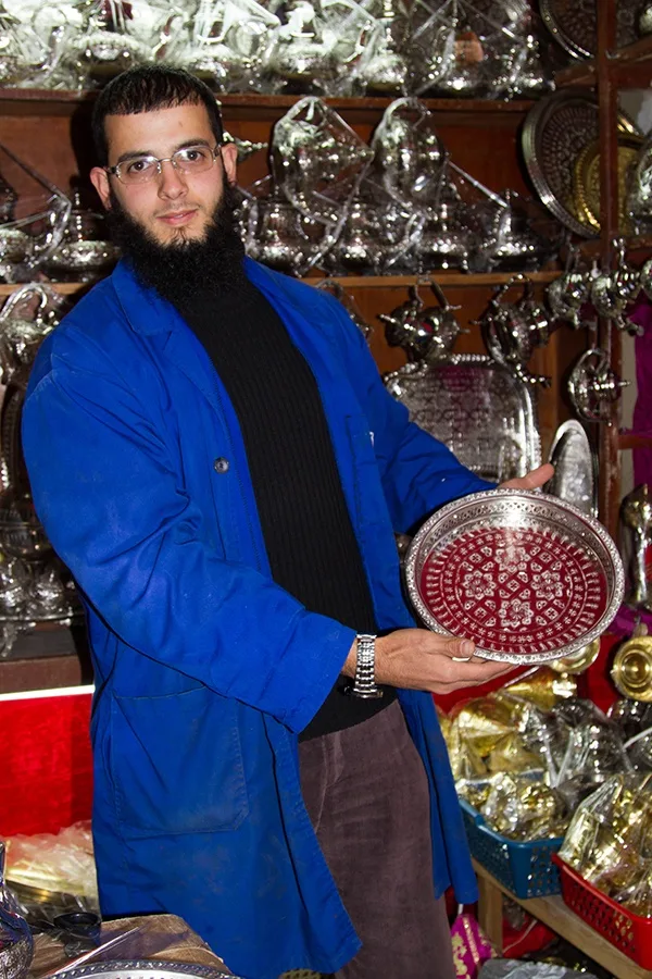 A silversmith in a bright blue lab coat holds a beautifully engraved silver bowl.