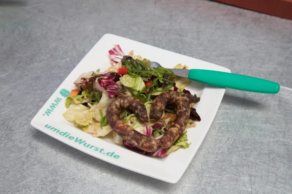 A heart-shaped bratwurst and salad on a plate.